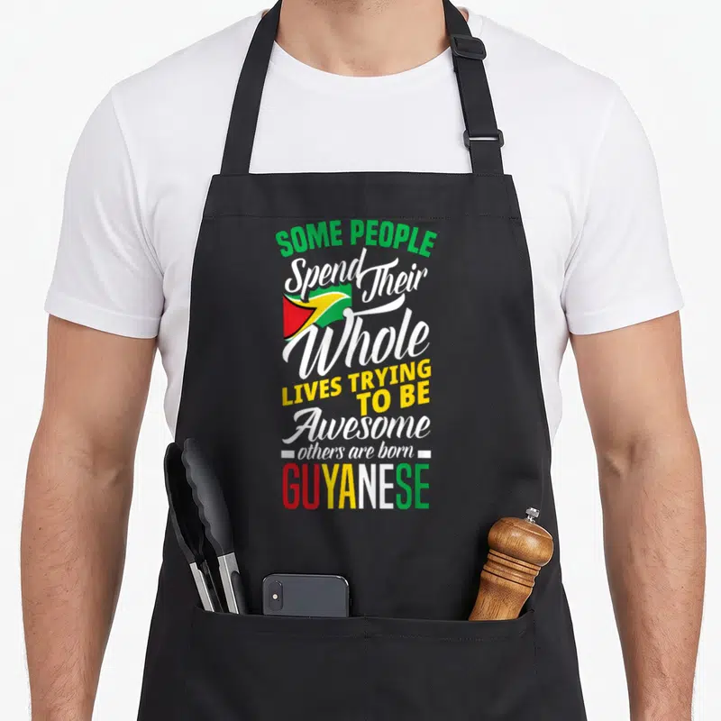 Cute guyanese guyana apron - Stacked text reading born GUYANESE with small flag in green yellow red and white — shown on a black cotton canvas apron against a white background