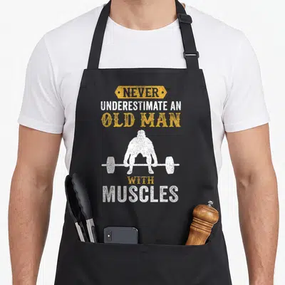 Funny weightlifting bodybuilder apron - Distressed yellow and white text above and below a white silhouette of a man — shown on a black cotton canvas apron against a white background