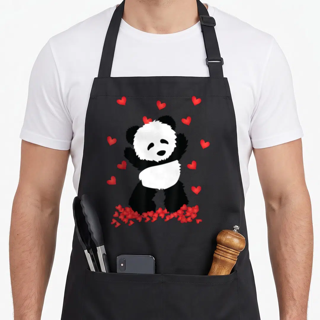 Panda valentine's day apron - Cartoon panda standing among scattered and clustered red hearts in black white and red — shown on a black cotton canvas apron against a white background
