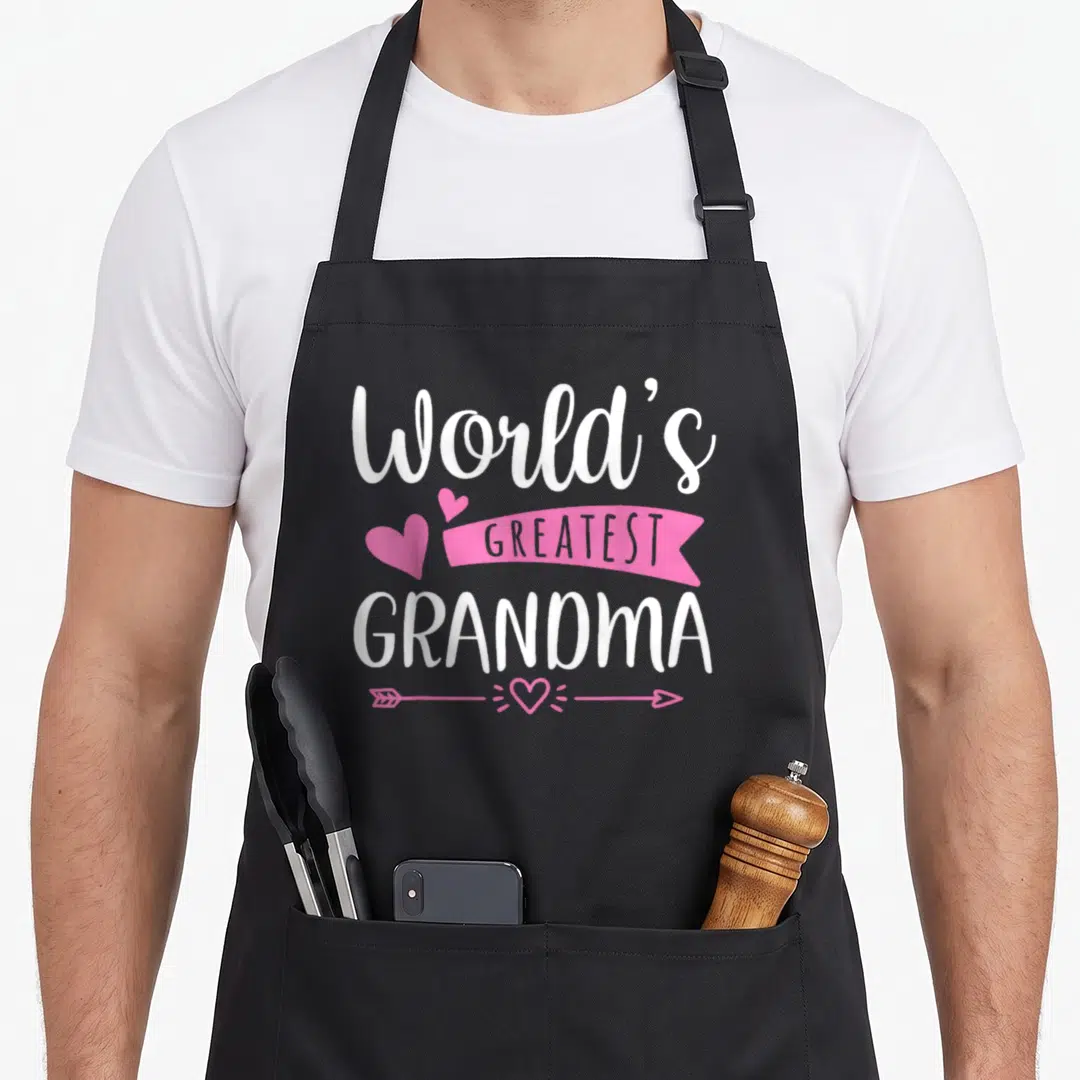 Mother worlds greatest dad apron - Stacked white text reading World's Greatest Grandma with pink ribbon hearts — shown on a black cotton canvas apron against a white background
