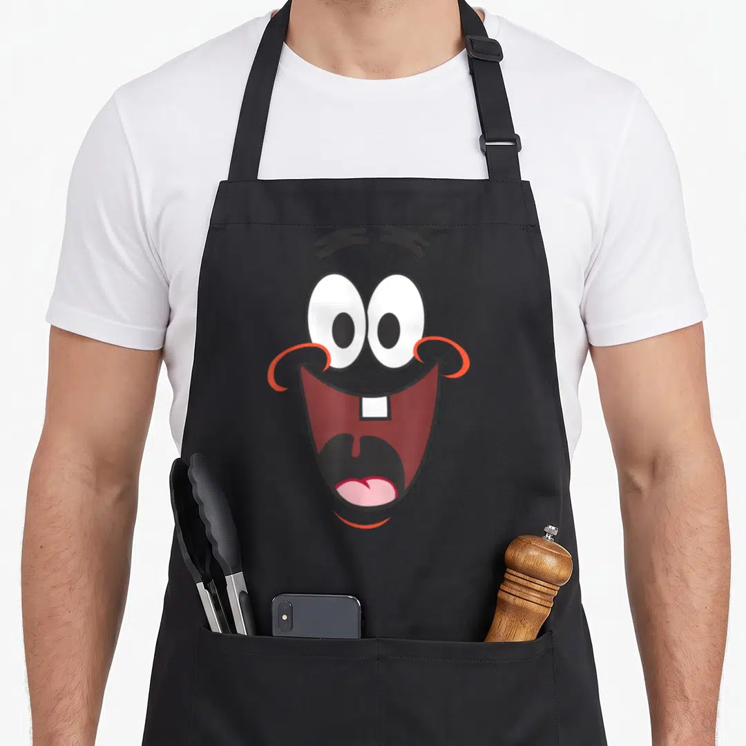 Squarepant face on apron - Cartoon face with wide open mouth and large eyes in white red black and pink — shown on a black cotton canvas apron against a white background