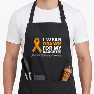 Daughter manuscript apron - Orange ribbon next to stacked text reading I Wear Orange For My Daughter with small heart — shown on a black cotton canvas apron against a white background