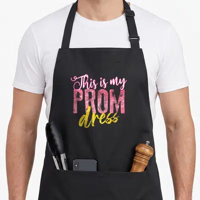 Promenade prom apron - Stacked pink and yellow typography reading This is my PROM dress — shown on a black cotton canvas apron against a white background