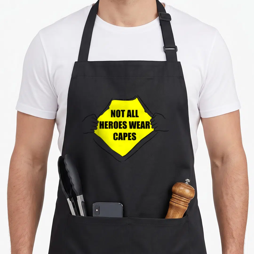 Heroe essential apron - Yellow shirt torn open by two hands revealing black text on grey background — shown on a black cotton canvas apron against a white background