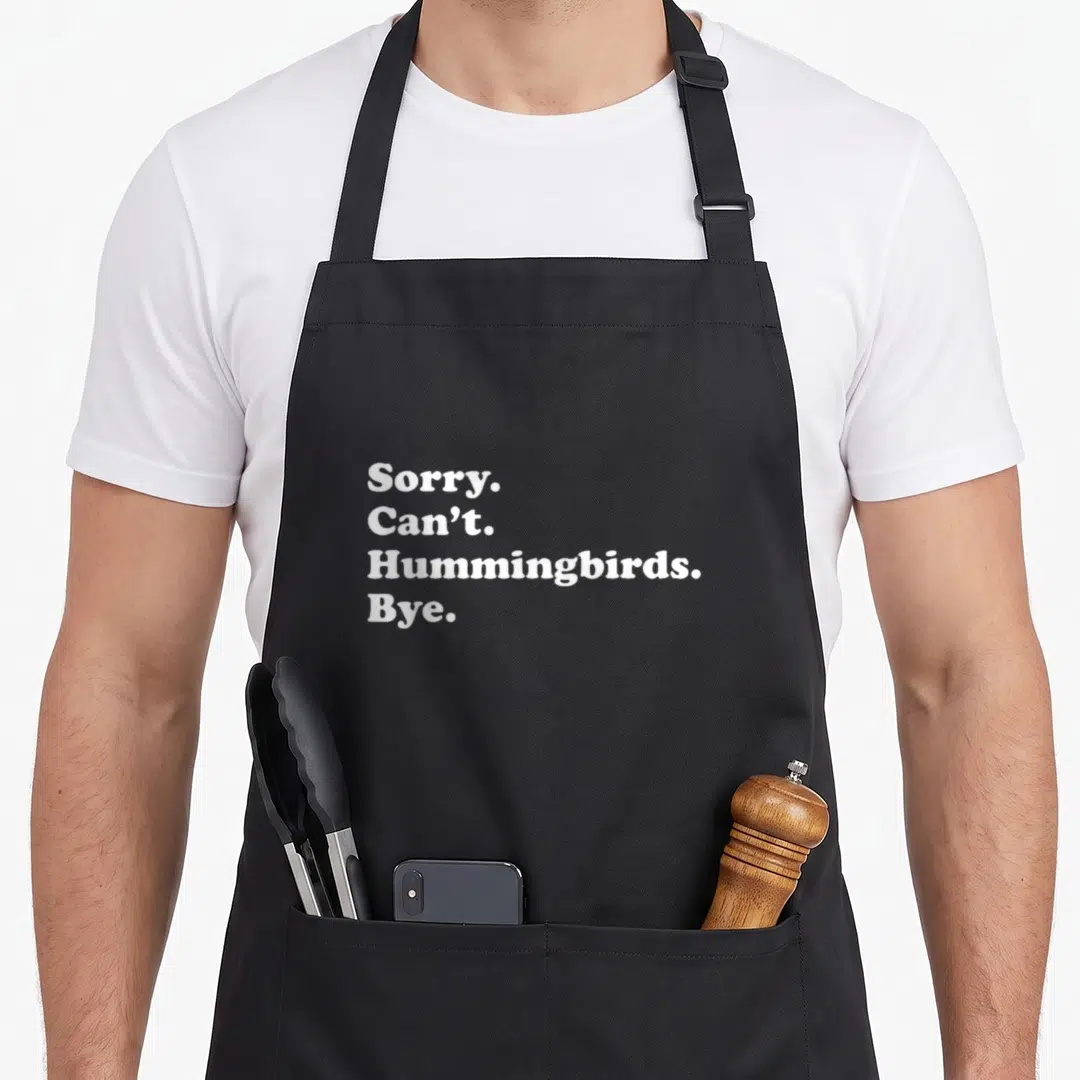 Retro hummingbird bird apron - White stacked text reading Sorry Can't Hummingbirds Bye on dark background — shown on a black cotton canvas apron against a white background