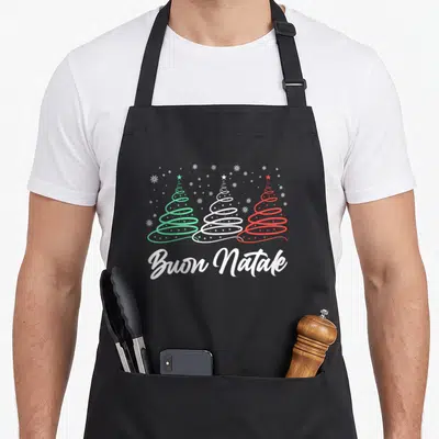 Natale italian aprons - Three spiral trees in green white red above Buon Natale script with scattered snowflakes — shown on a black cotton canvas apron against a white background
