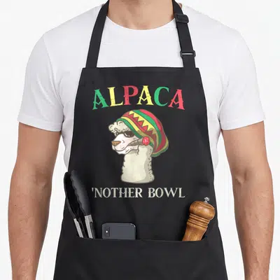 Grass alpaca apron - Cartoon alpaca in rasta beanie smoking with arched text ALPACA and bottom text Nother Bowl — shown on a black cotton canvas apron against a white background