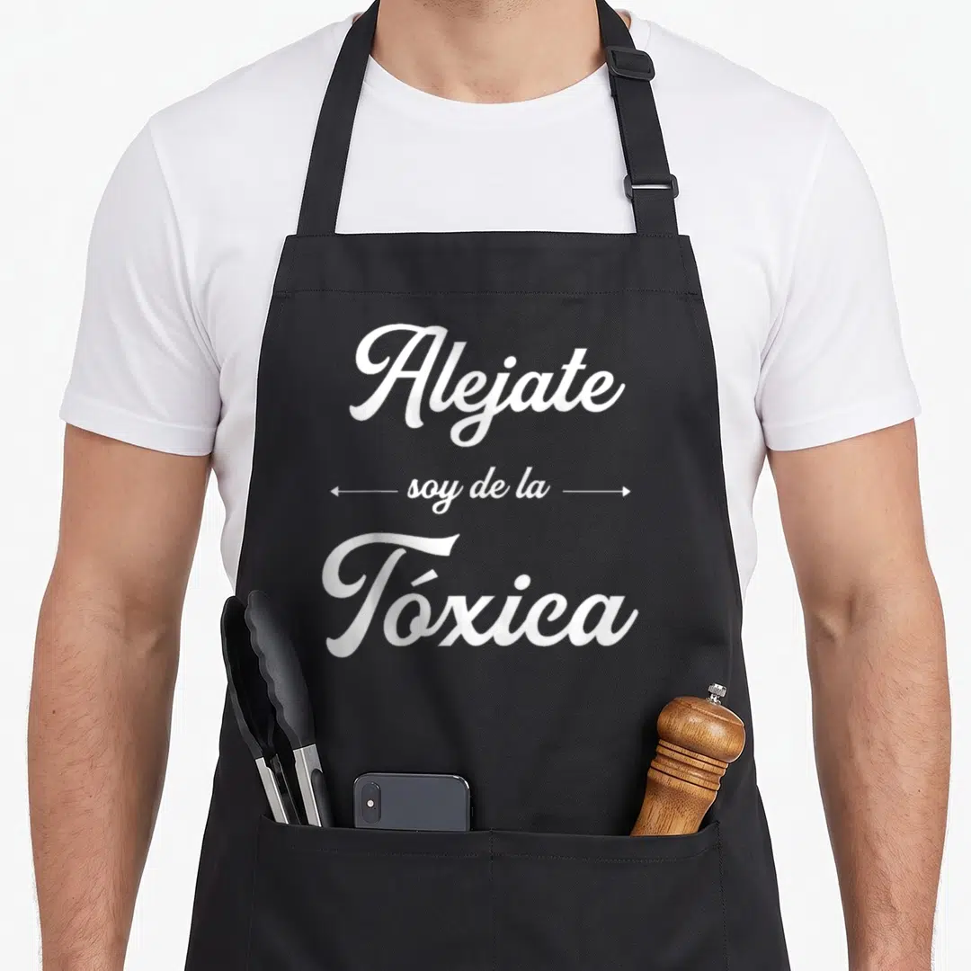 Alejate funny soy apron - White cursive text reading Alejate soy de la Tóxica with horizontal arrows — shown on a black cotton canvas apron against a white background