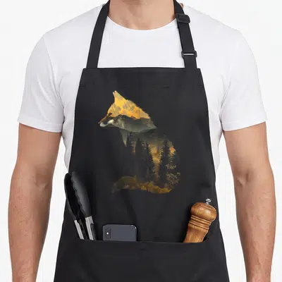 Forest fox print apron - Sitting fox silhouette filled with mountain range and pine forest in orange and grey — shown on a black cotton canvas apron against a white background