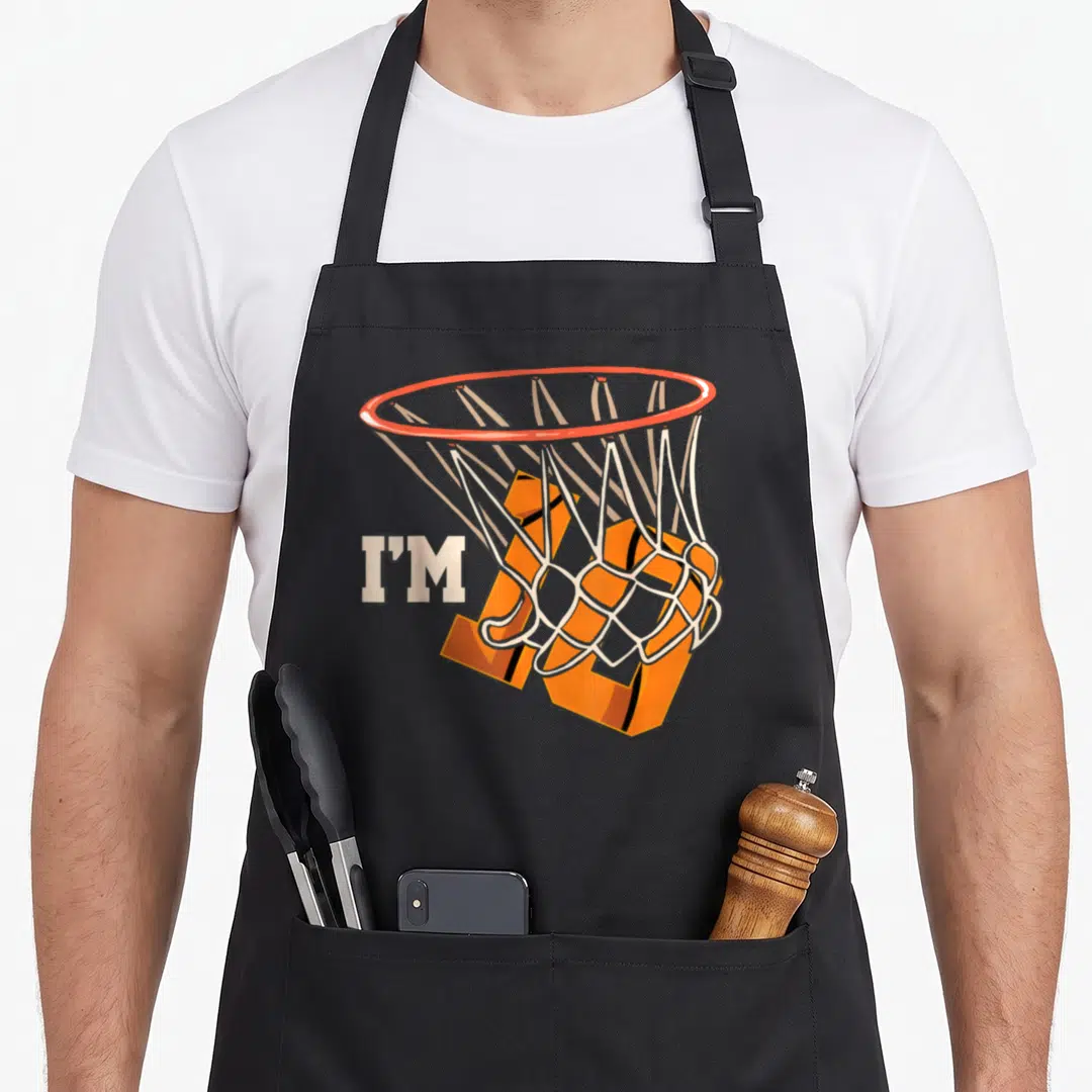 Basketball celebration birthday apron - I'M 10 text with orange basketball falling through white hoop net — shown on a black cotton canvas apron against a white background