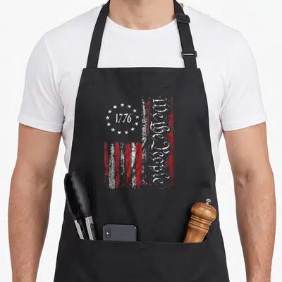 Vintage patriotic american flag apron - Distressed USA flag with 1776 in stars and vertical We the People text on red — shown on a black cotton canvas apron against a white background