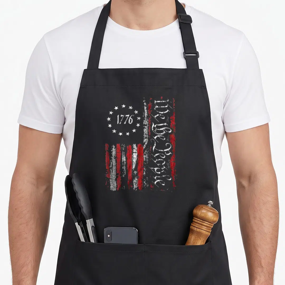 Vintage patriotic american flag apron - Distressed USA flag with 1776 in stars and vertical We the People text on red — shown on a black cotton canvas apron against a white background
