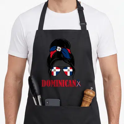 Dominicana messy bun apron - Cartoon woman bun with Dominican flag sunglasses and DOMINICAN text in red blue white black — shown on a black cotton canvas apron against a white background
