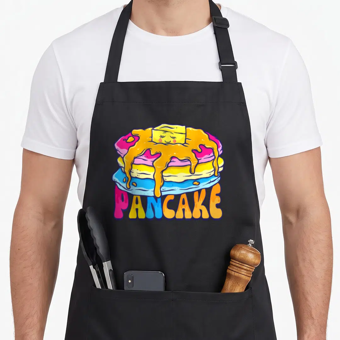 Pansexual pancake apron - Cartoon stack of three pink yellow and blue pancakes with butter and orange syrup, PANCAKE — shown on a black cotton canvas apron against a white background