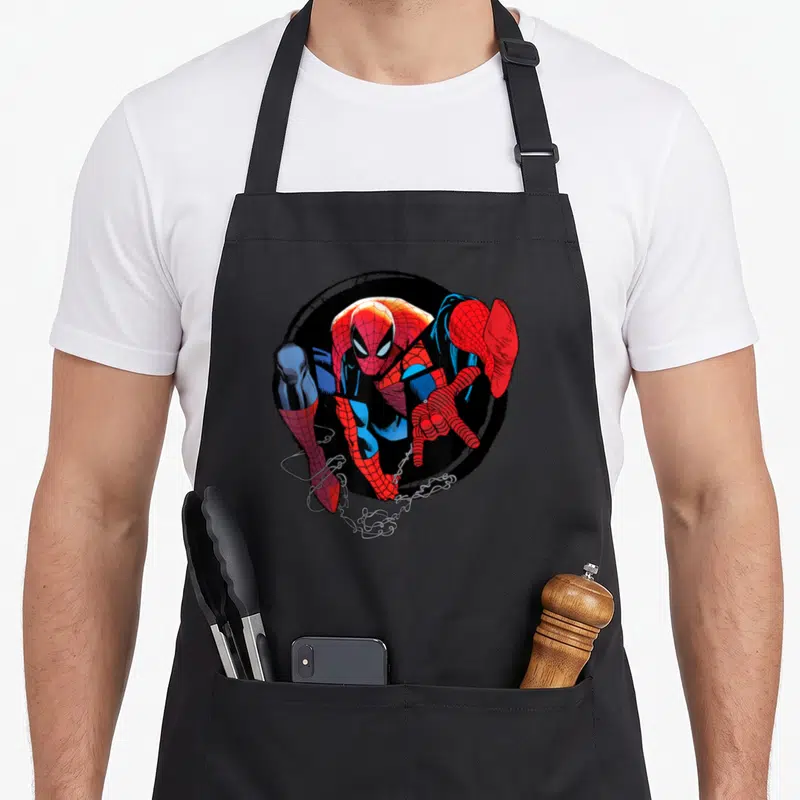 Web amazing aprons - Spider-Man in red blue and black circle with white webbing extending from bottom left — shown on a black cotton canvas apron against a white background