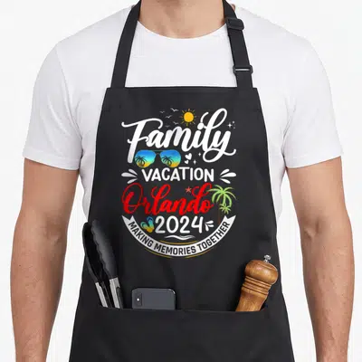 Vacation orlando family aprons - Stacked text reading Family Vacation Orlando 2024 with sunglasses and palm tree — shown on a black cotton canvas apron against a white background