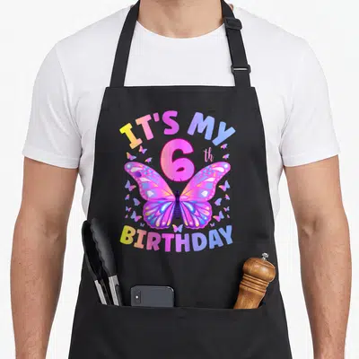Six butterfly aprons - Rainbow butterfly and 6th birthday text on pink purple blue yellow canvas — shown on a black cotton canvas apron against a white background