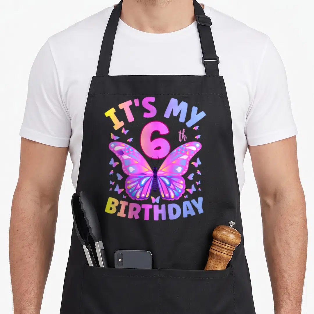 Six butterfly aprons - Rainbow butterfly and 6th birthday text on pink purple blue yellow canvas — shown on a black cotton canvas apron against a white background