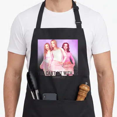 Sit us aprons - Photo of three women in pink with text YOU CAN'T SIT WITH US MEAN GIRLS — shown on a black cotton canvas apron against a white background