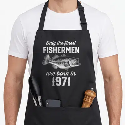 55th fishing aprons - Distressed white bass illustration with text Only the finest FISHERMEN are born in 1971 — shown on a black cotton canvas apron against a white background