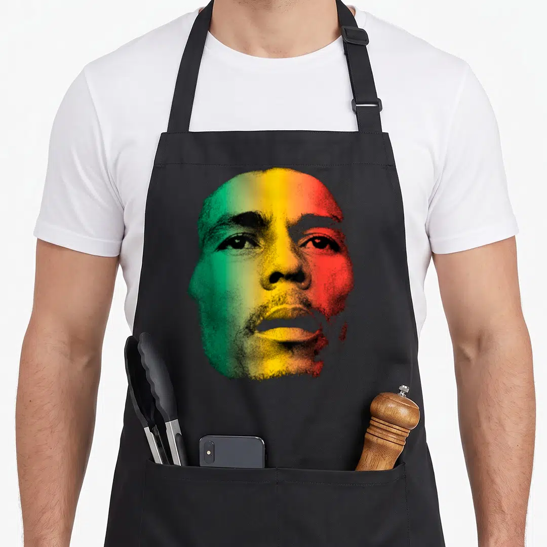 Bob face apron - Stylized face portrait in green yellow red and black on black background — shown on a black cotton canvas apron against a white background