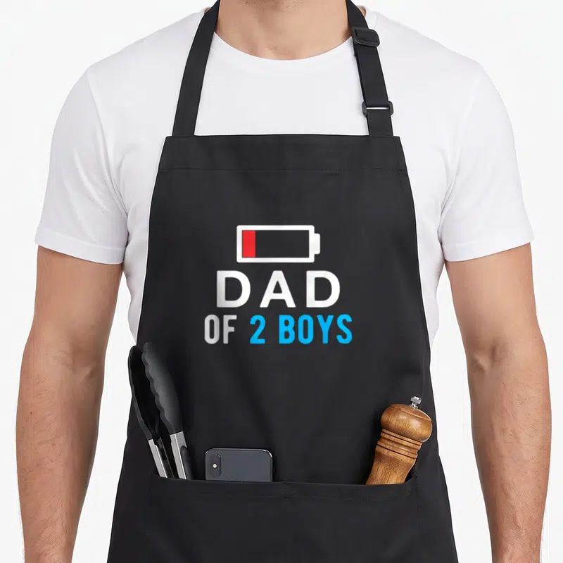 Cool father day apron - Low battery icon above Dad of 2 Boys text in white red and blue — shown on a black cotton canvas apron against a white background