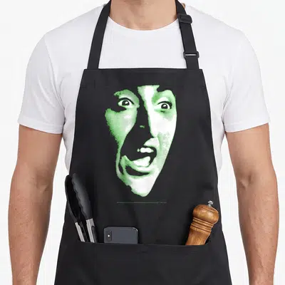 Wizard witch apron - Stylized green and white face print on apron with two front pockets — shown on a black cotton canvas apron against a white background