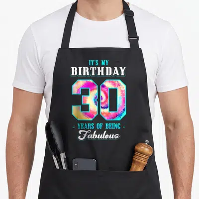 Birthday thirty funny dirty aprons - Tie-dye number 30 with IT'S MY BIRTHDAY 30 YEARS OF BEING Fabulous text in pink — shown on a black cotton canvas apron against a white background