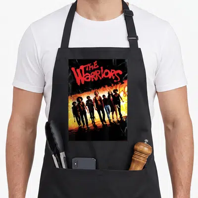 Poster curry apron - Red The Warriors text above seven men walking against orange and yellow background — shown on a black cotton canvas apron against a white background