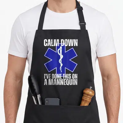 Funny mannequin emt apron - Blue Star of Life with distressed white text reading Calm Down I've Done This On A Mannequin — shown on a black cotton canvas apron against a white background