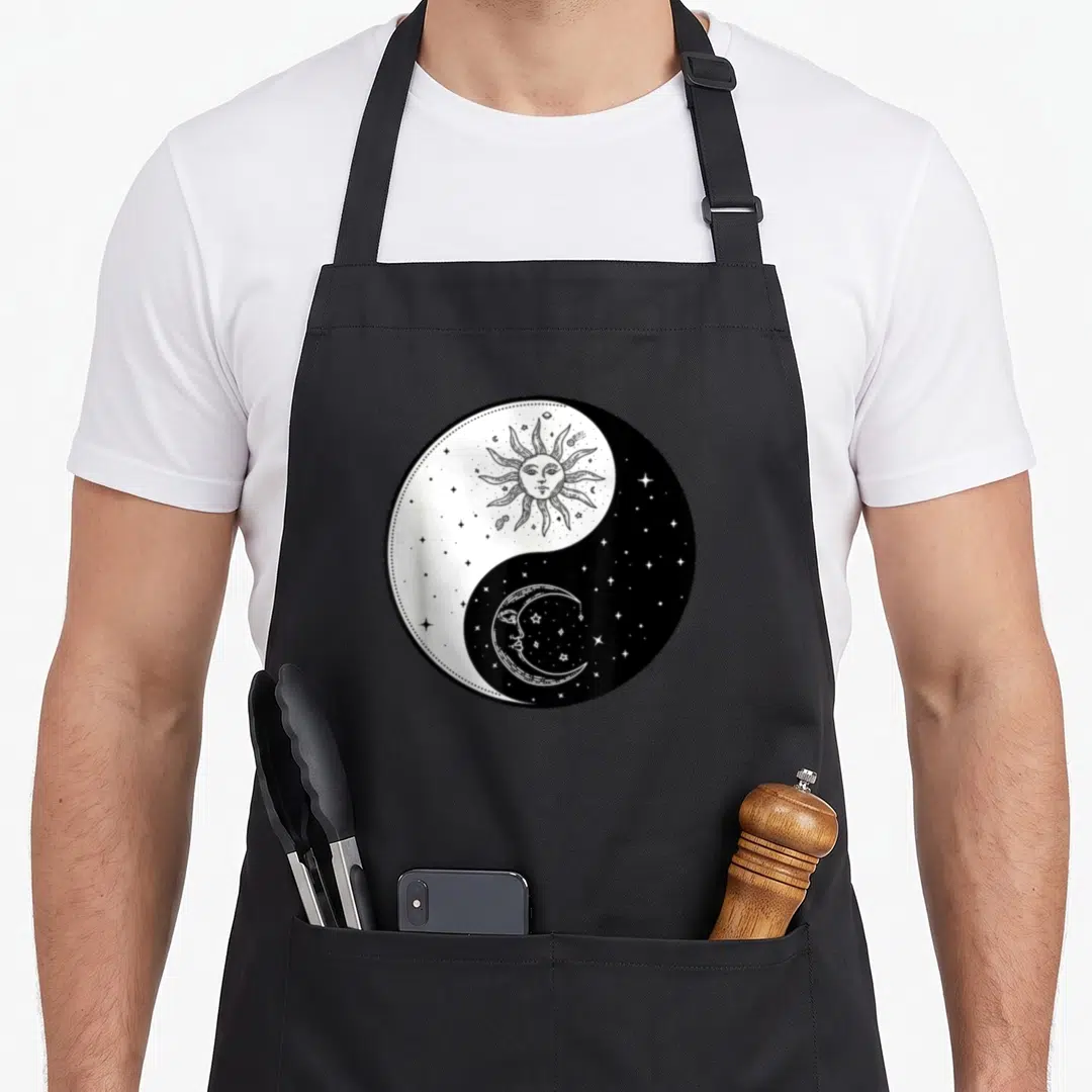 Sun moon child apron - Yin yang symbol with sun face in white and moon face in black surrounded by scattered stars — shown on a black cotton canvas apron against a white background