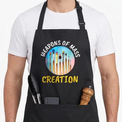 Painting artist painter apron - Eight colorful paintbrushes in a circle with Weaprons of Mass Creation text — shown on a black cotton canvas apron against a white background