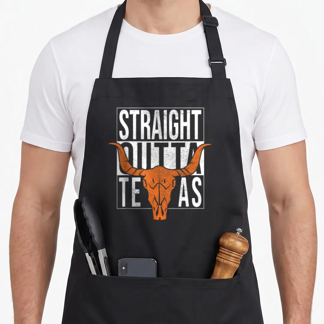 Straight texans apron - Orange bull skull over distressed white text STRAIGHT OUTTA TEXAS in rectangular frame — shown on a black cotton canvas apron against a white background
