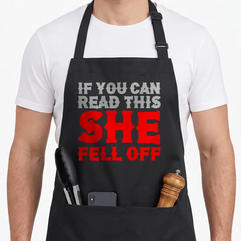 Read biker apron - Red and grey typography reading If You Can Read This She Fell Off — shown on a black cotton canvas apron against a white background