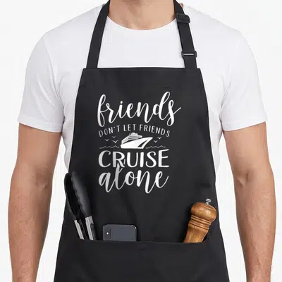 Alone friends apron - White typography reading friends don't let friends cruise alone with ship and wave graphic — shown on a black cotton canvas apron against a white background