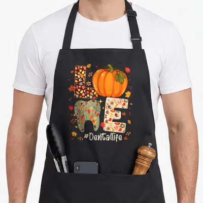 Dental thanksgiving apron - LOVE spelled with patterned L, pumpkin O, tooth V, beige E, and #Dentallife hashtag below — shown on a black cotton canvas apron against a white background