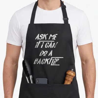 Ask backflip parkour apron - White stacked text ASK ME if i CAN DO A BACKFLIP on black background — shown on a black cotton canvas apron against a white background