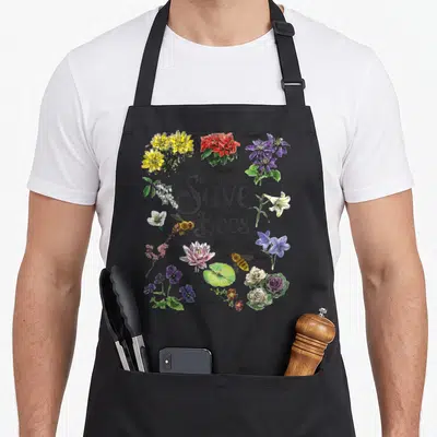 Botanical bee apron - Save The Bees text surrounded by labeled botanical illustrations of flowers and bees in color — shown on a black cotton canvas apron against a white background