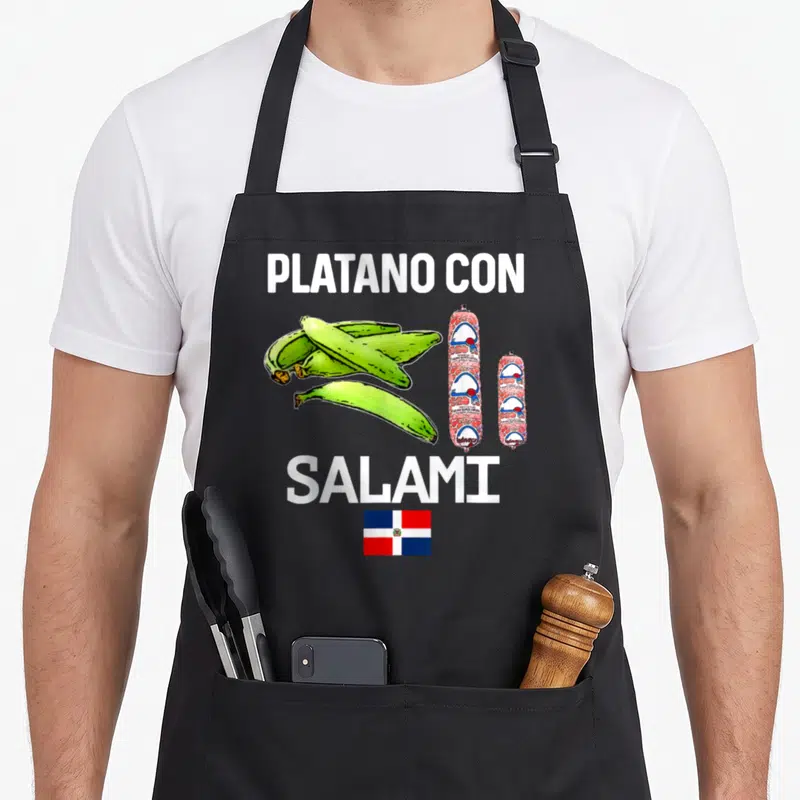 Dominicana food aprons - PLATANO CON SALAMI text with green plantains, two salami sticks, and Dominican Republic flag — shown on a black cotton canvas apron against a white background