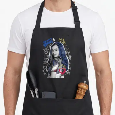 Evie novelty apron - Photo of Evie with BEAUTY & BRAINS text, gold crowns, red heart, and white stars — shown on a black cotton canvas apron against a white background