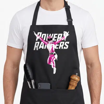 Pose karate apron - Pink ranger character jumping in front of white power rangers text — shown on a black cotton canvas apron against a white background