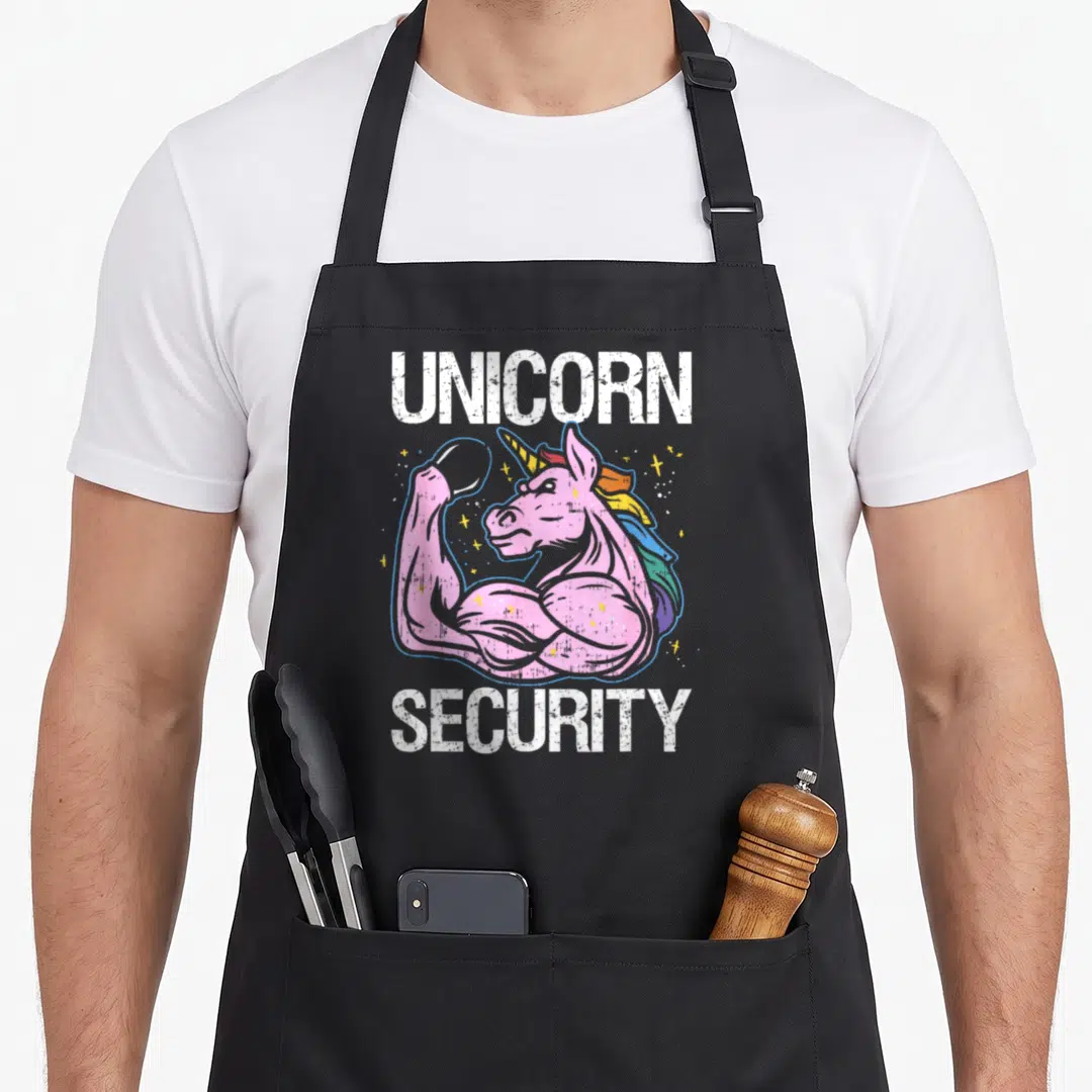 Security halloween apron - Pink cartoon unicorn flexing muscles between UNICORN and SECURITY text with yellow stars — shown on a black cotton canvas apron against a white background