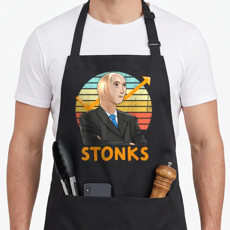 Stonk stock aprons - Cartoon man in suit with blue tie and orange arrow above STONKS text on striped background — shown on a black cotton canvas apron against a white background
