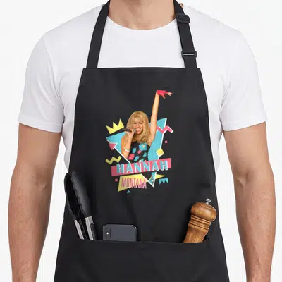 Hannah 90s apron - HANNAH MONTANA text banners with woman and pink blue yellow geometric shapes — shown on a black cotton canvas apron against a white background