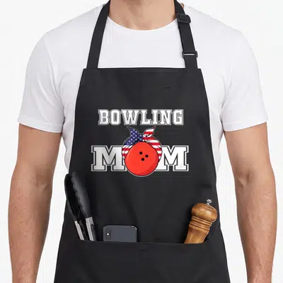 Cute bowling player apron - Red bowling ball in US flag headband between white BOWLING MOM letters — shown on a black cotton canvas apron against a white background