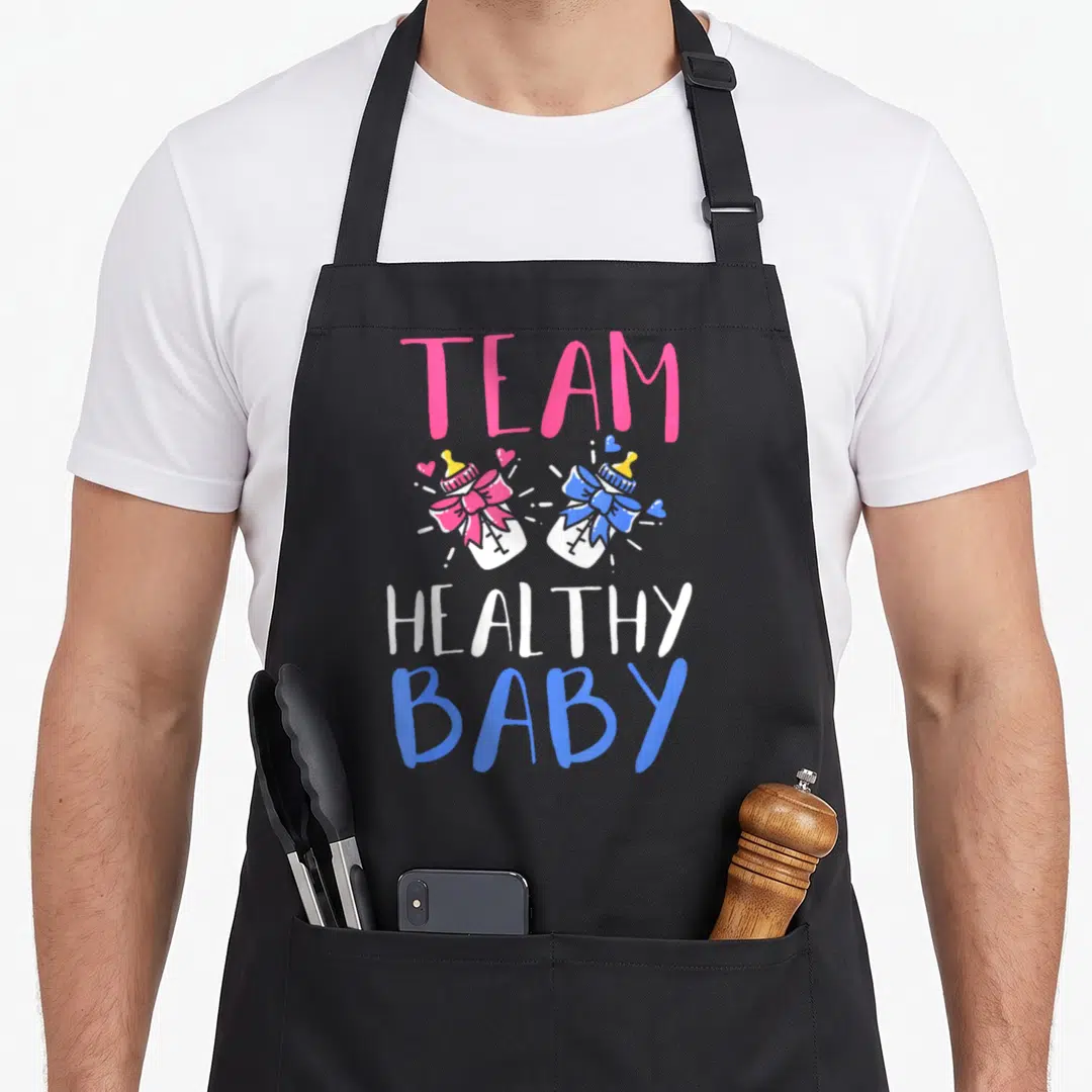 Gender healthy apron - TEAM HEALTHY BABY text with pink and blue decorated baby bottles in cartoon style — shown on a black cotton canvas apron against a white background
