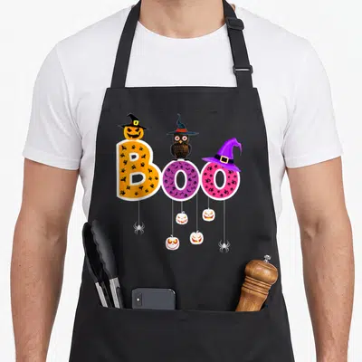 Boo halloween witch apron - Colorful BOO text with icons, witch hat pumpkin, owl, and hanging jack-o-lanterns — shown on a black cotton canvas apron against a white background