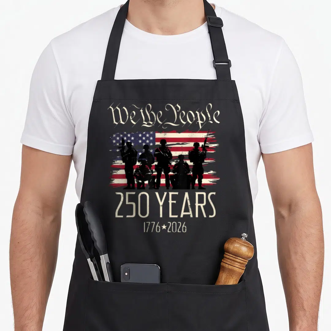 250th american flag apron - Five black soldier silhouettes standing before distressed red white blue flag with We — shown on a black cotton canvas apron against a white background