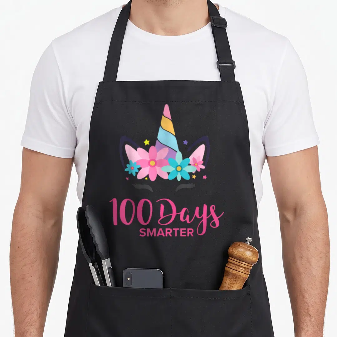 School costume unicorn apron - Cartoon unicorn head with flower crown and 100 Days Smarter text in pink — shown on a black cotton canvas apron against a white background