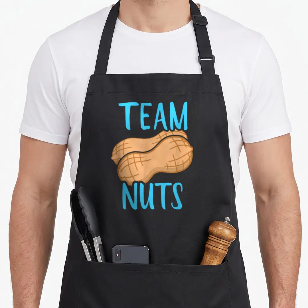 Reveal family aprons - Blue TEAM NUTS text surrounding two overlapping tan peanuts on black fabric — shown on a black cotton canvas apron against a white background